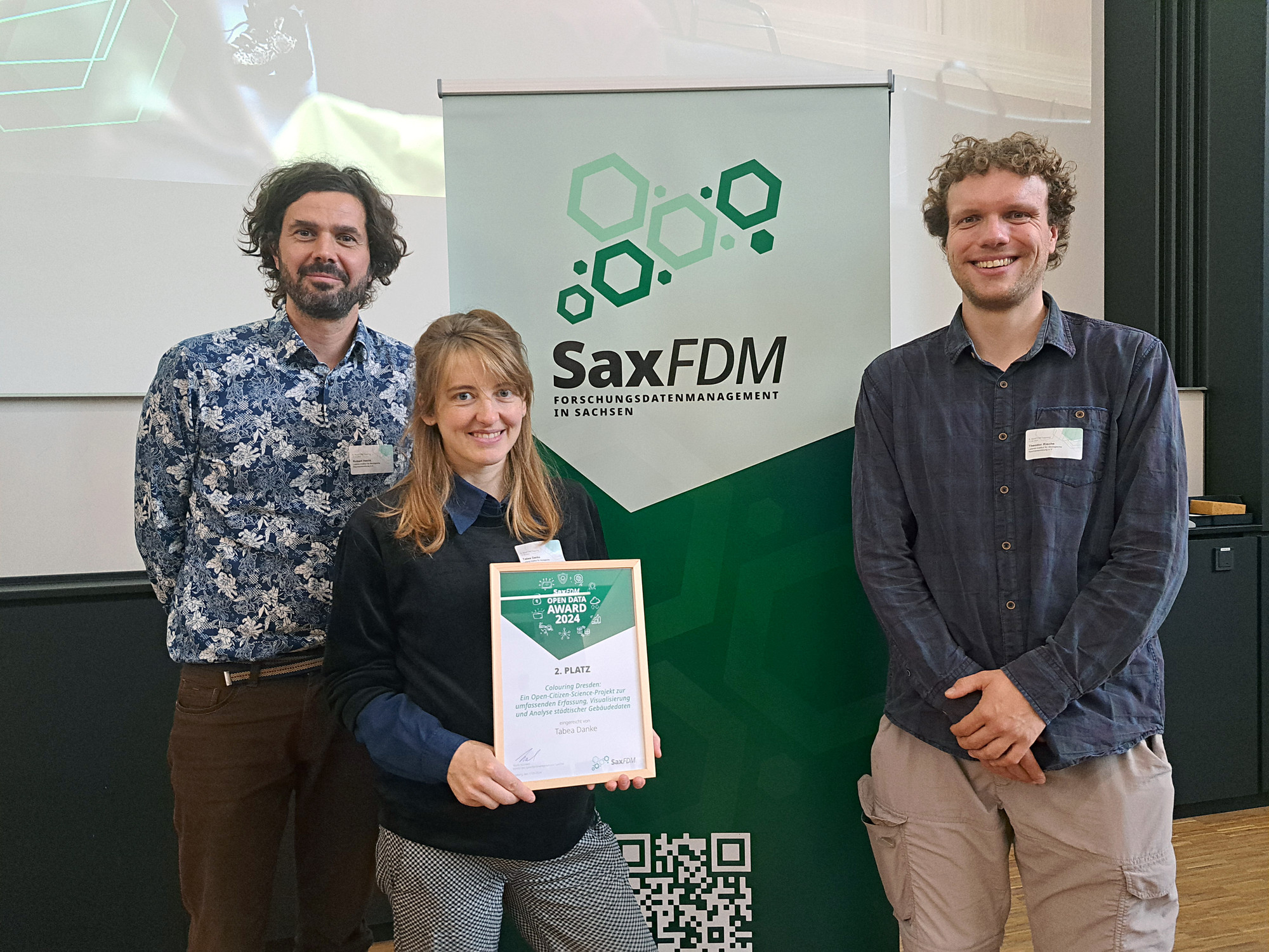 Auf dem sieht man das Projektteam mit einem Award des 2. Platzes vor einem Aufsteller mit der Aufschrift "SaxFDM Forschungsdatenmanagement in Sachsen".